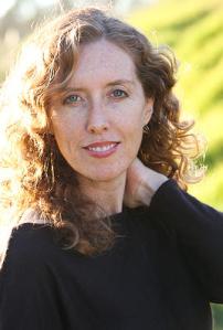 Author photo, shoulder-length curly light brown hair, wearing a dark crew neck sweater